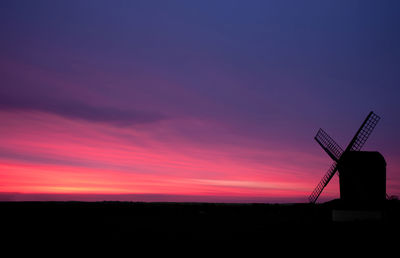 Traditional windmill on field against sky during sunset