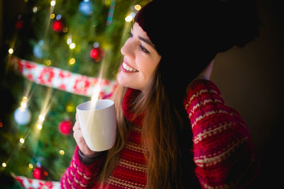 Young woman drinking coffee cup on christmas tree