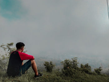 Side view of young man sitting on land