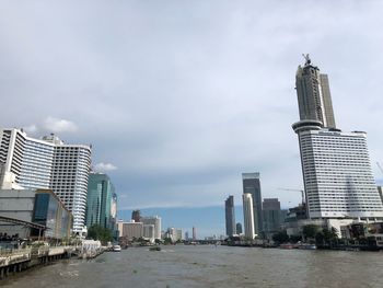 Modern buildings by river against sky in city