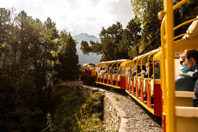 Small tourist train with people moving on railroad through mountains in summer day in pyrenees