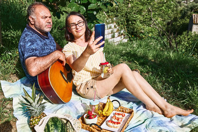 Middle aged couple having a picnic in the garden with fresh exotic fruit and sweet sandwiches.