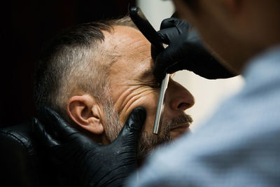 Barber cutting beard of man at salon