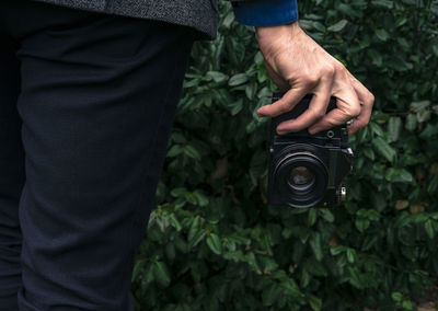 Midsection of man holding camera against plants