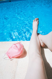 Low section of woman with mask sitting at poolside