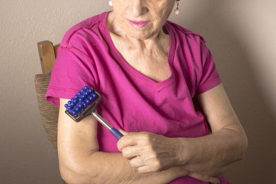 Midsection of woman using massager while sitting at home