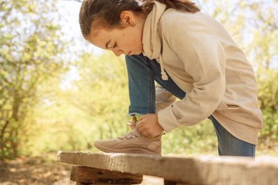 Child tying up laces his sneakers in spring park for walk. girl ties bow on her shoe outdoors.