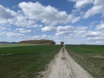Dirt road amidst field against sky in eichsfeld, thuringia, germany