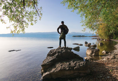 Man standing on rock by sea against clear sky