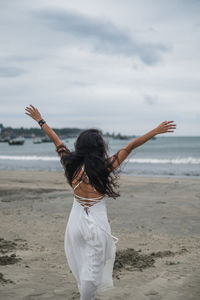 Woman with arms raised on beach against sky