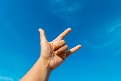 Cropped hand gesturing horn sign against blue sky