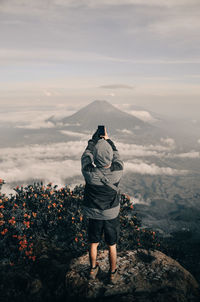 Rear view of man standing on mountain against sky