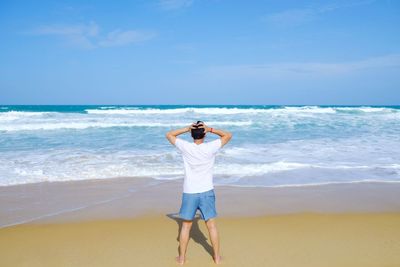 Rear view of man standing at beach against sky
