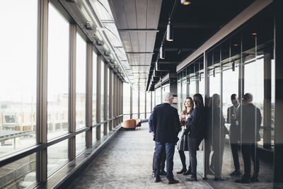 Smiling female entrepreneur talking to colleagues in office corridor