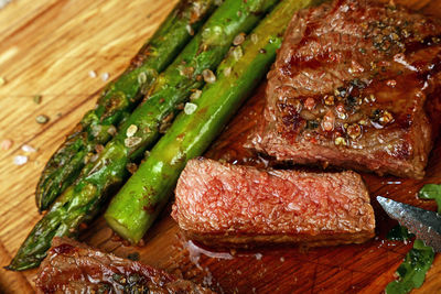 High angle view of grilled beef steak and asparagus on wooden plate