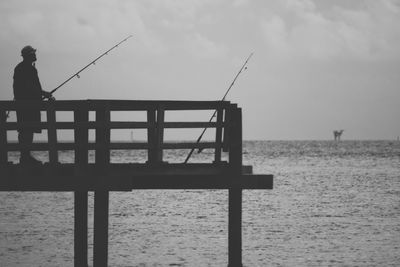 Man fishing on pier at sea against sky