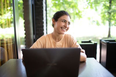 Smiling woman using laptop while sitting at cafe