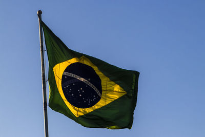 Brazilian flag flutters on a flagpole with the blue sky in the background