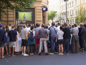 Rear view of people standing on street in city, outdoor screening football