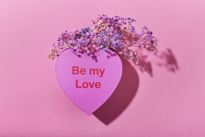 Heart-shaped box and flowers on pink background