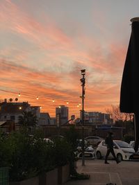 Cars on road by buildings against sky during sunset