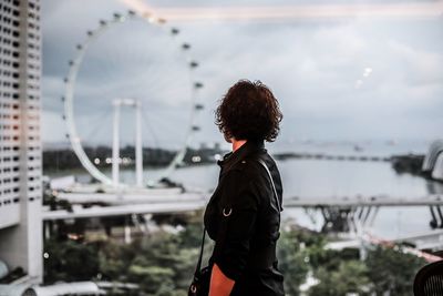 Rear view of woman standing in amusement park against sky