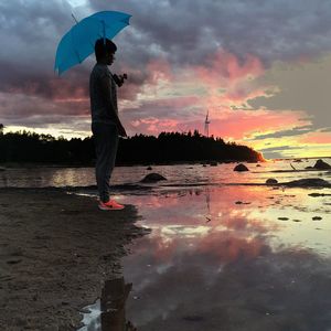 Man standing on beach against sky during sunset