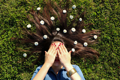 Directly above view of woman covering eyes while lying with flowers on hair at park