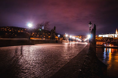 Illuminated city by river against sky at night