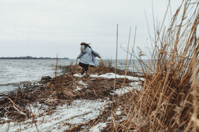 Man walking on snow covered land against sky