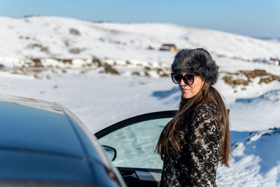 Portrait of woman standing by car on snow covered land