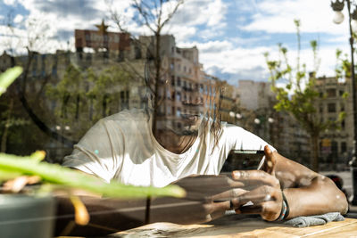 Man using mobile phone seen through window at table