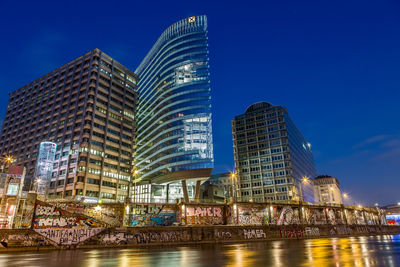 Low angle view of illuminated skyscrapers against blue sky