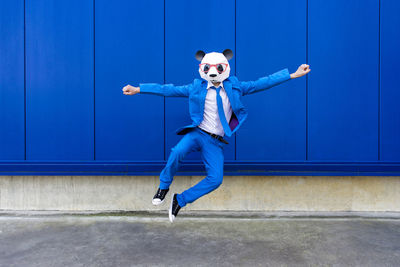 Full length of boy jumping against blue wall