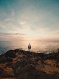 Rear view of man standing on beach against sky during sunset