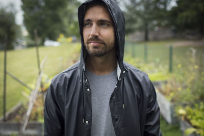 Thoughtful mid adult man wearing raincoat in vegetable garden