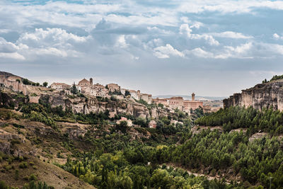 Scenic view of medieval town cuenca with old stone houses located on hills covered with green trees under blue cloudy sky in summer day in spain
