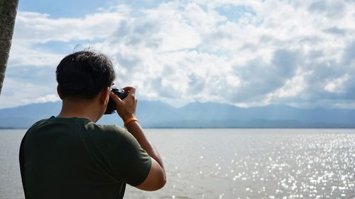 Rear view of man photographing on mountain against sky