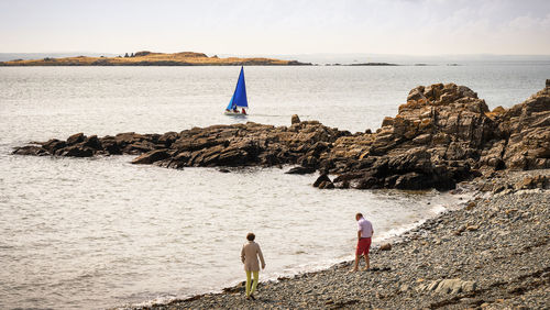 People on rock by sea against sky