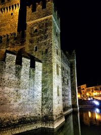 Illuminated building by river against sky at night