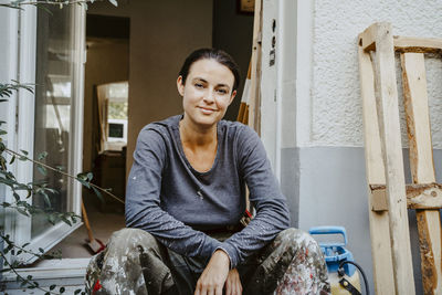 Portrait of smiling female carpenter sitting in front of house entrance