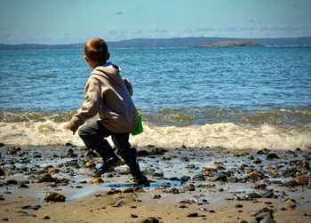 Rear view of boy on beach against sky