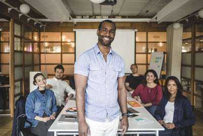 Portrait of confident businessman standing by colleagues sitting in board room at office