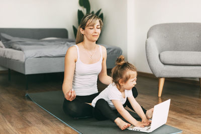 A beautiful young woman and her adorable little daughter smile and meditate after a workout together