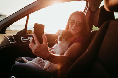 Portrait of smiling woman sitting in car with dog during sunset