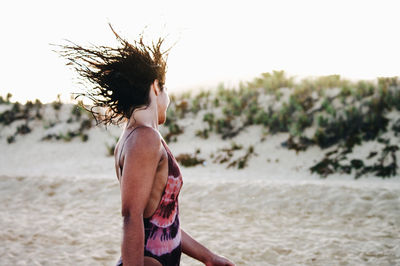 Young woman tossing hair while standing on sand at beach