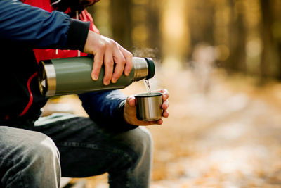 Close-ups of a man pouring tea into a cup from a thermos while relaxing in an autumn park or forest