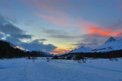 Snow covered landscape against sky during sunset