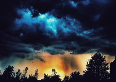 Low angle view of silhouette trees against dramatic sky