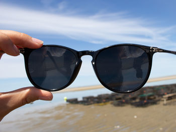 Close-up of hand holding sunglasses against sky